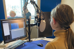 Een Club Orange lid ervaart hoe het inspreken in een studio werkt. Ze zit achter de microfoon.