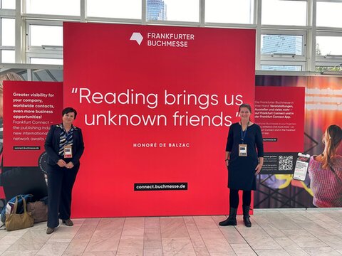 Twee experts van Dedicon poseren voor een grote poster in de Frankfurter Buchmesse. De tekst op de poster: