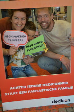 Drie personen kijken door fotolijst met daarop de tekst Achter iedere Dediconner staat een fantastische familie