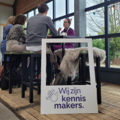 Een bord met 'Wij zijn kennismakers' staat tegen een statafel waar mensen aan zitten te lunchen